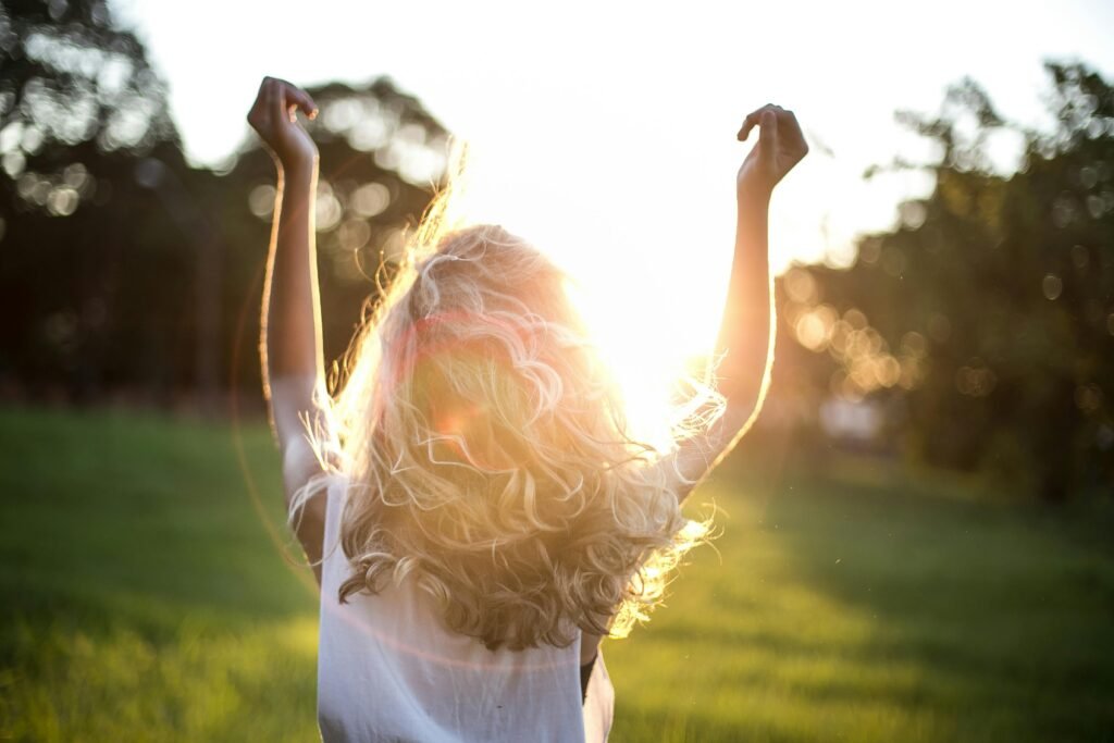 pexels-photo-852793-852793 A woman with outstretched arms celebrates the sunset in a grassy field, capturing the essence of freedom and joy.